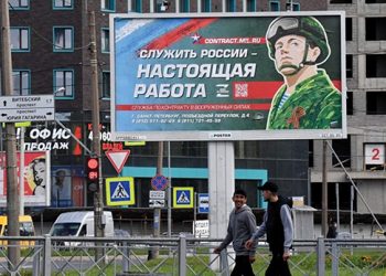 Young men walk by a sign saying “To Serve Russia is the real job” in Saint Petersburg. Source: AFP