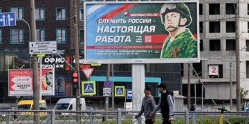 Young men walk by a sign saying “To Serve Russia is the real job” in Saint Petersburg. Source: AFP