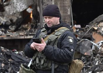 A Ukrainian police officer checks his smartphone following a missile strike in Kyiv. Source: AFP