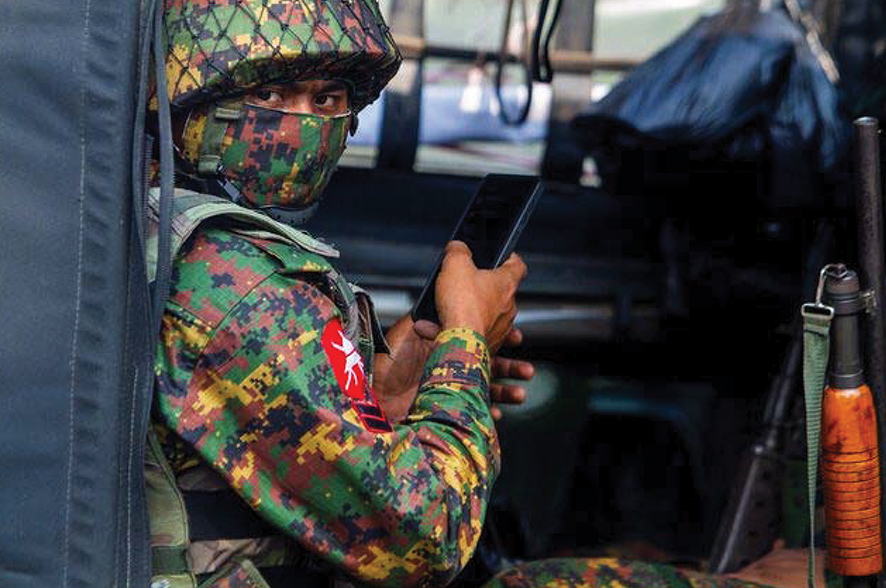 A soldier uses a mobile phone as he sits inside a military vehicle outside Myanmar's Central Bank during a protest against the military coup, in Yangon, Myanmar, February 15, 2021. Source: REUTERS/Stringer/File Photo/File Photo