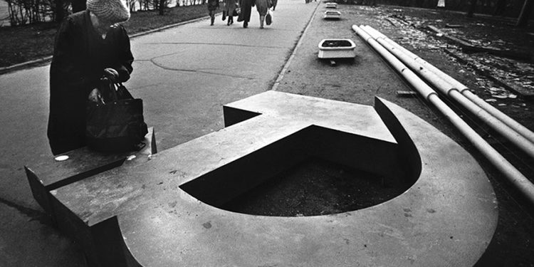 A woman reaches into her bag, which rests on a fallen Soviet hammer-and-sickle on a Moscow street in 1991. Source: The Atlantic
