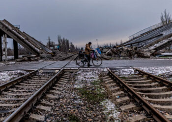 A man in Pokrovsk carries his belongings on a bicycle past a bridge destroyed by Russian shelling. Photo by Anton Shtuka for NPR