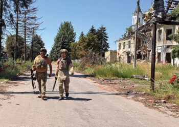 Ukrainian servicemen in full gear walk along a road past a building destroyed by shelling in June. Photo by Alex Nikitenko/Global Images Ukraine via Getty Images
